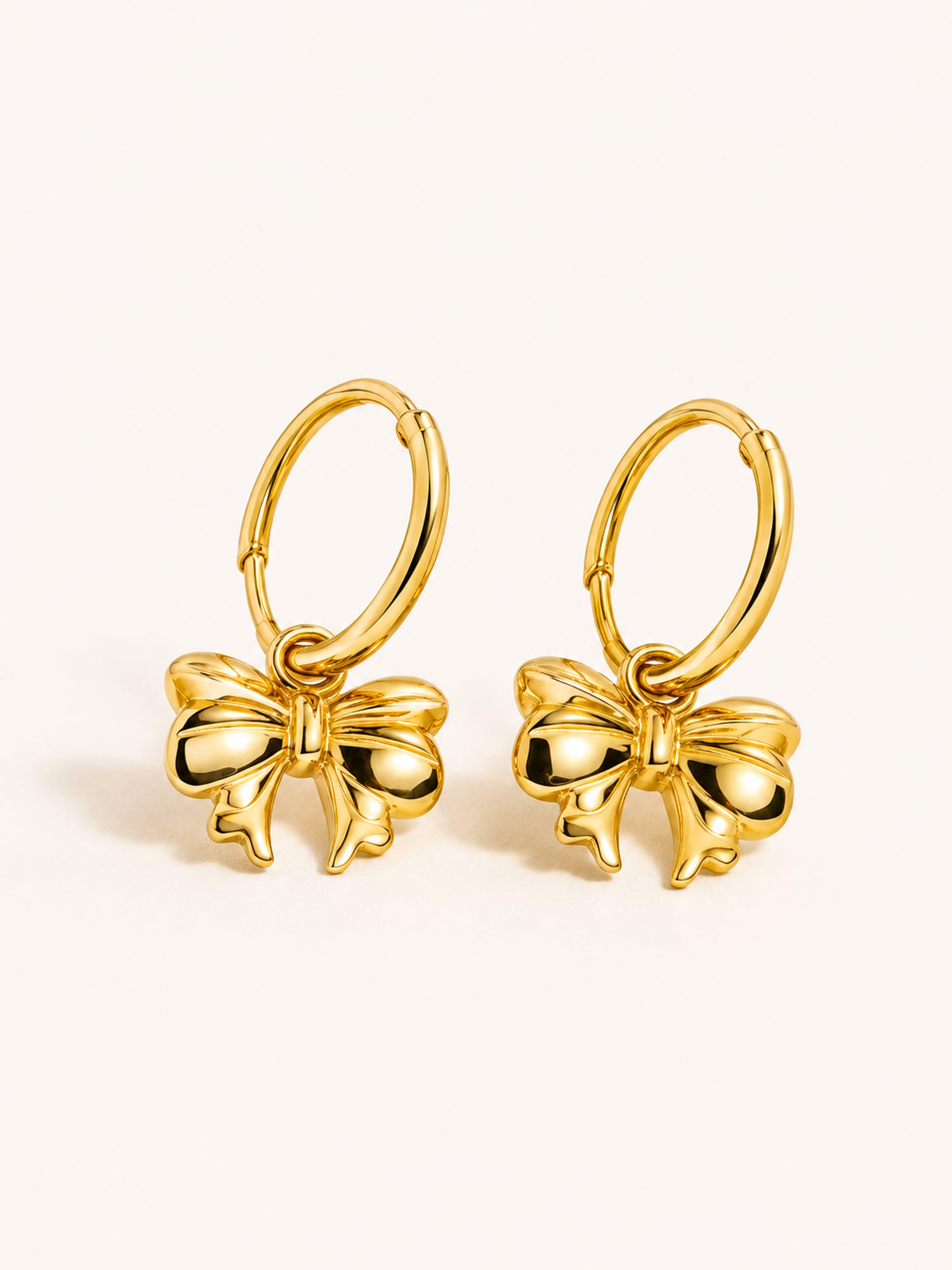 Gold bow charm hoop earrings in polished stainless steel with a minimalist feminine design.