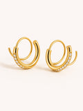 A pair of gold-toned double-hoop earrings with a row of small clear stones along the front curve, shown on a plain light beige background.