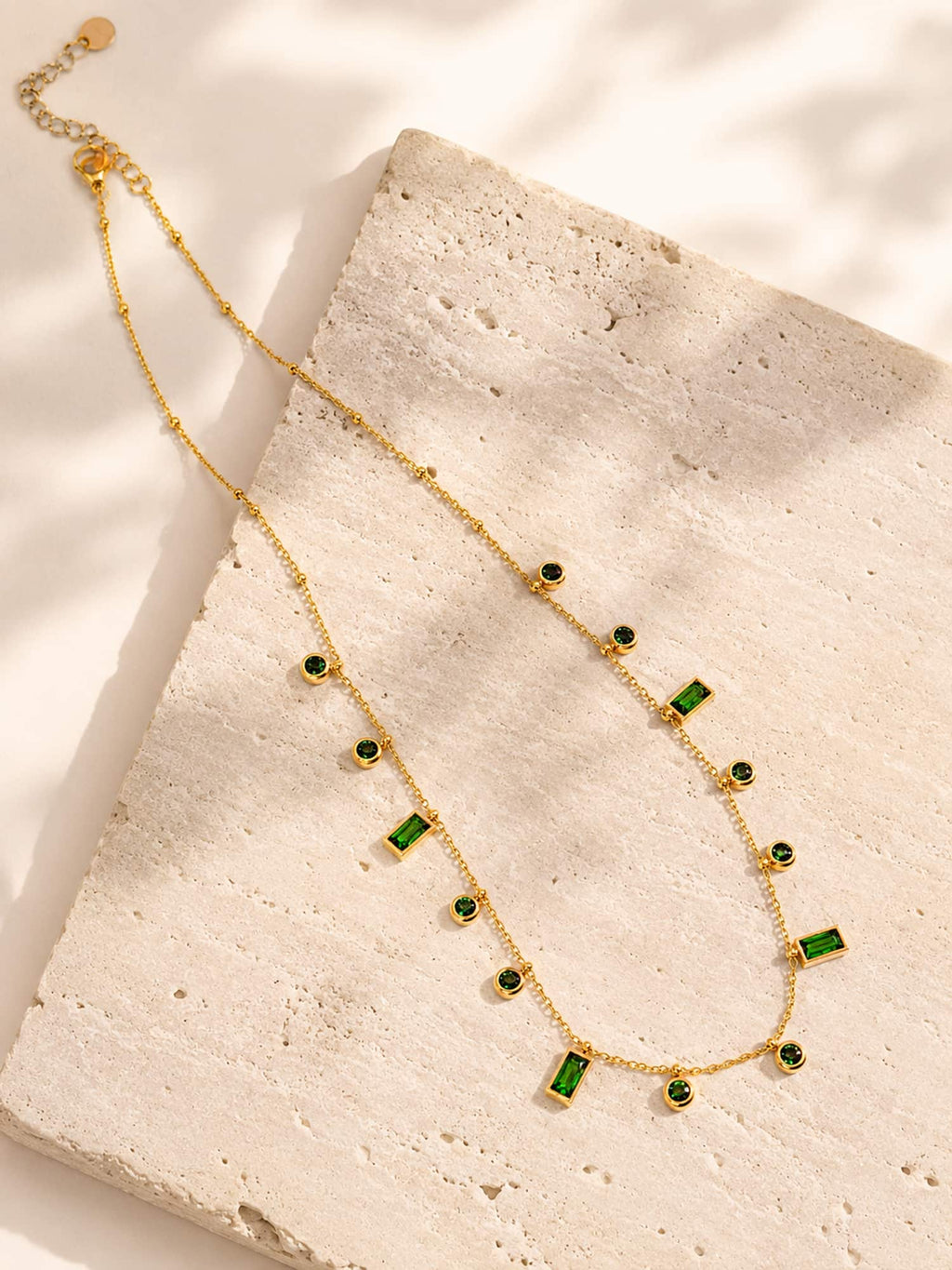 Minimalist green CZ station necklace displayed on a textured stone surface showcasing mixed-cut emerald green stones.