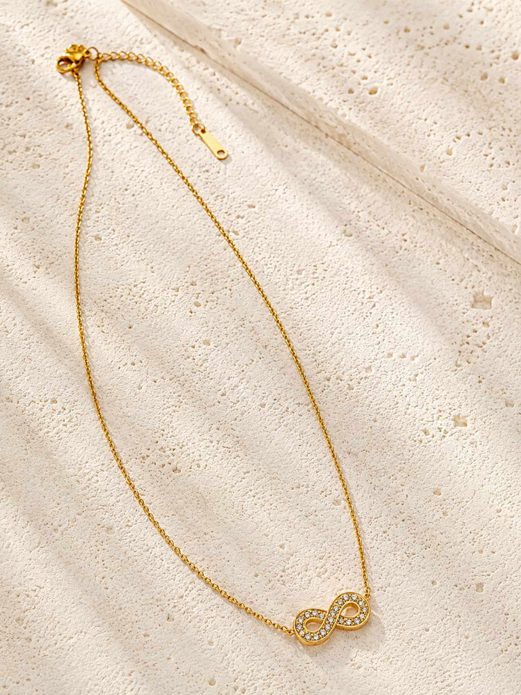 Infinity CZ pendant necklace displayed on a textured stone surface with a delicate gold chain.