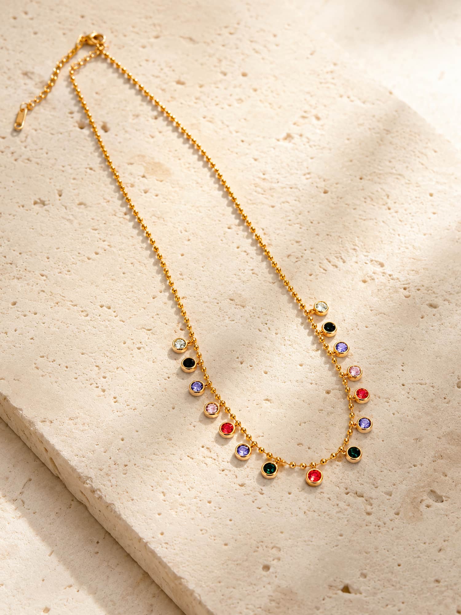 Minimalist multicolor bezel station necklace flat lay on textured stone surface