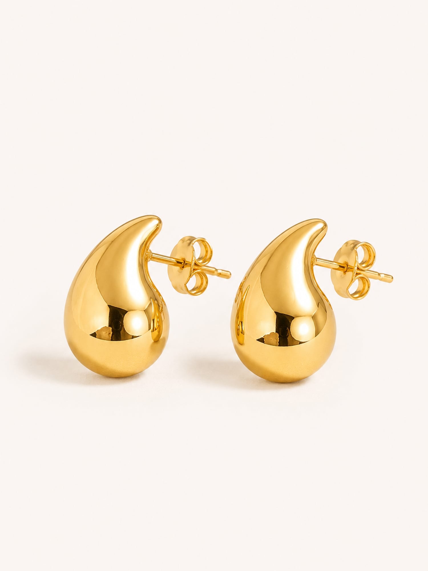 Polished gold teardrop stud earrings in stainless steel with a sculptural minimalist design.